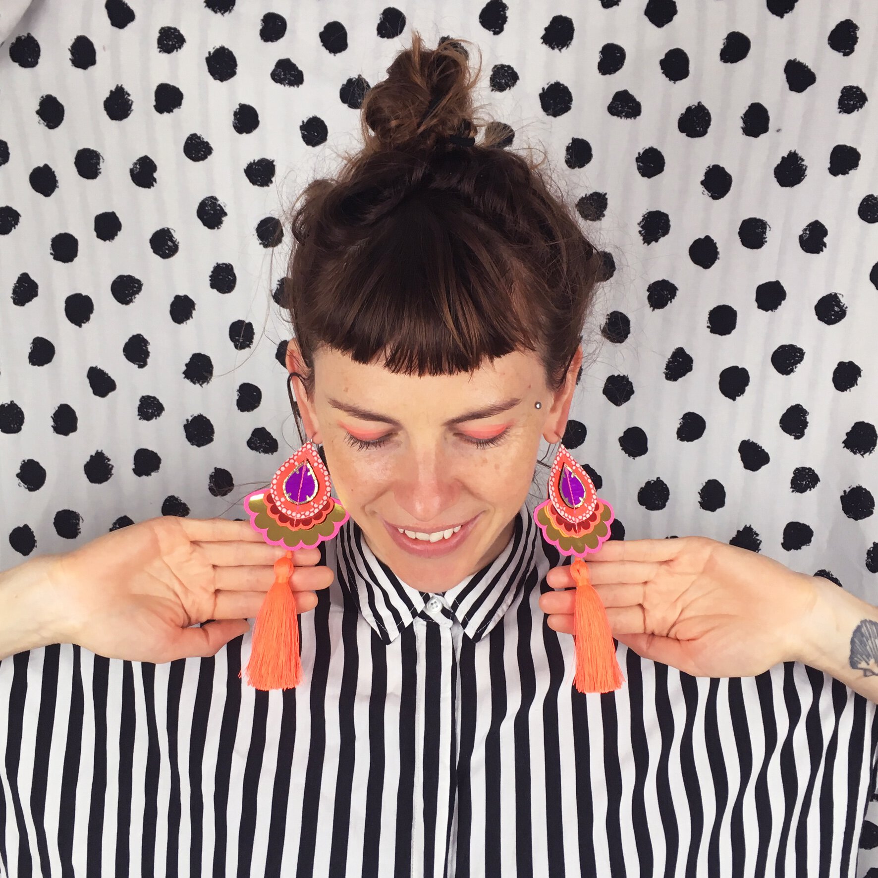 dakota rae dust designer bec denton wearing a monochrome striped shirt against a black and white polka dot wall, wearing fluorescent statement tassel earrings