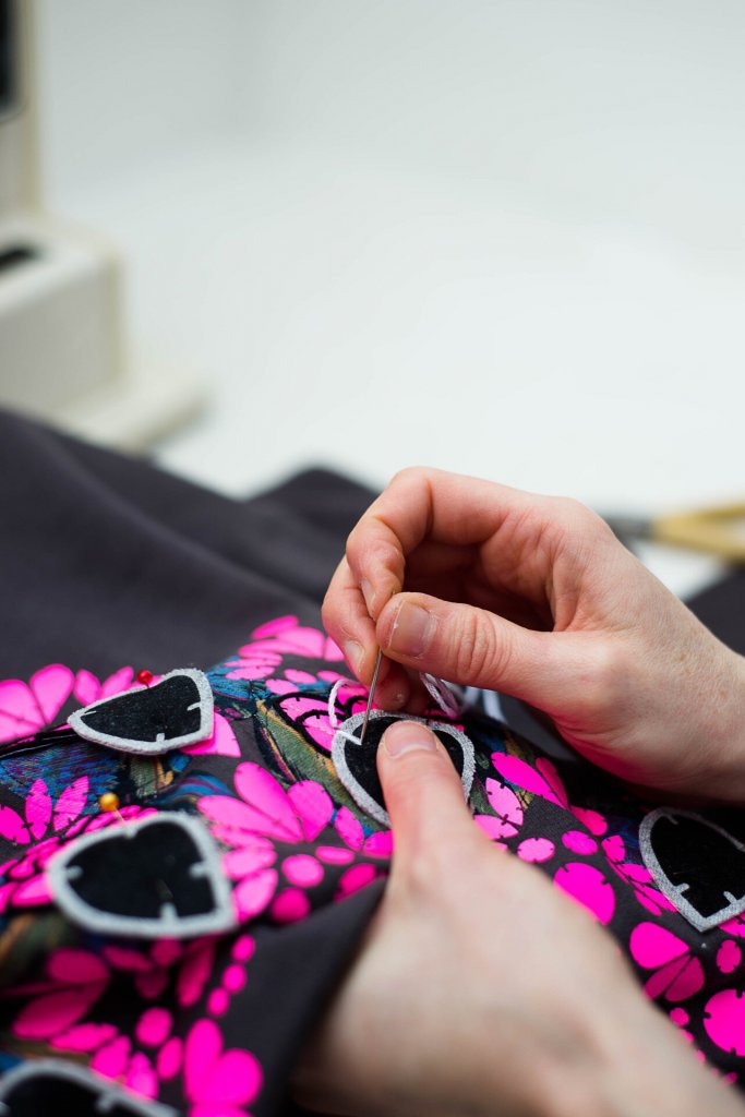 Bec Denton's hands, stitching an embellished sweatshirt. Grey with a neon pink print