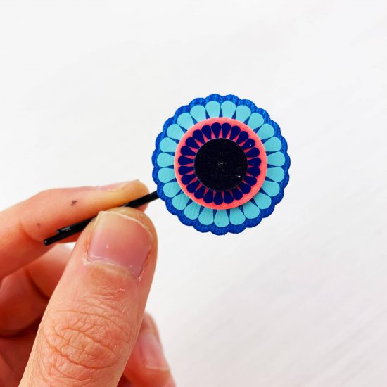 A single decorative charm hair pin held close to the camera, with a hand for scale