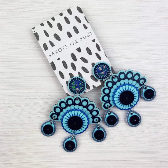 Blue chandelier style statement earrings displayed on a patterned card.