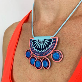Neon coral and blue, jangly charm necklace worn by a model in a bright neon red vest