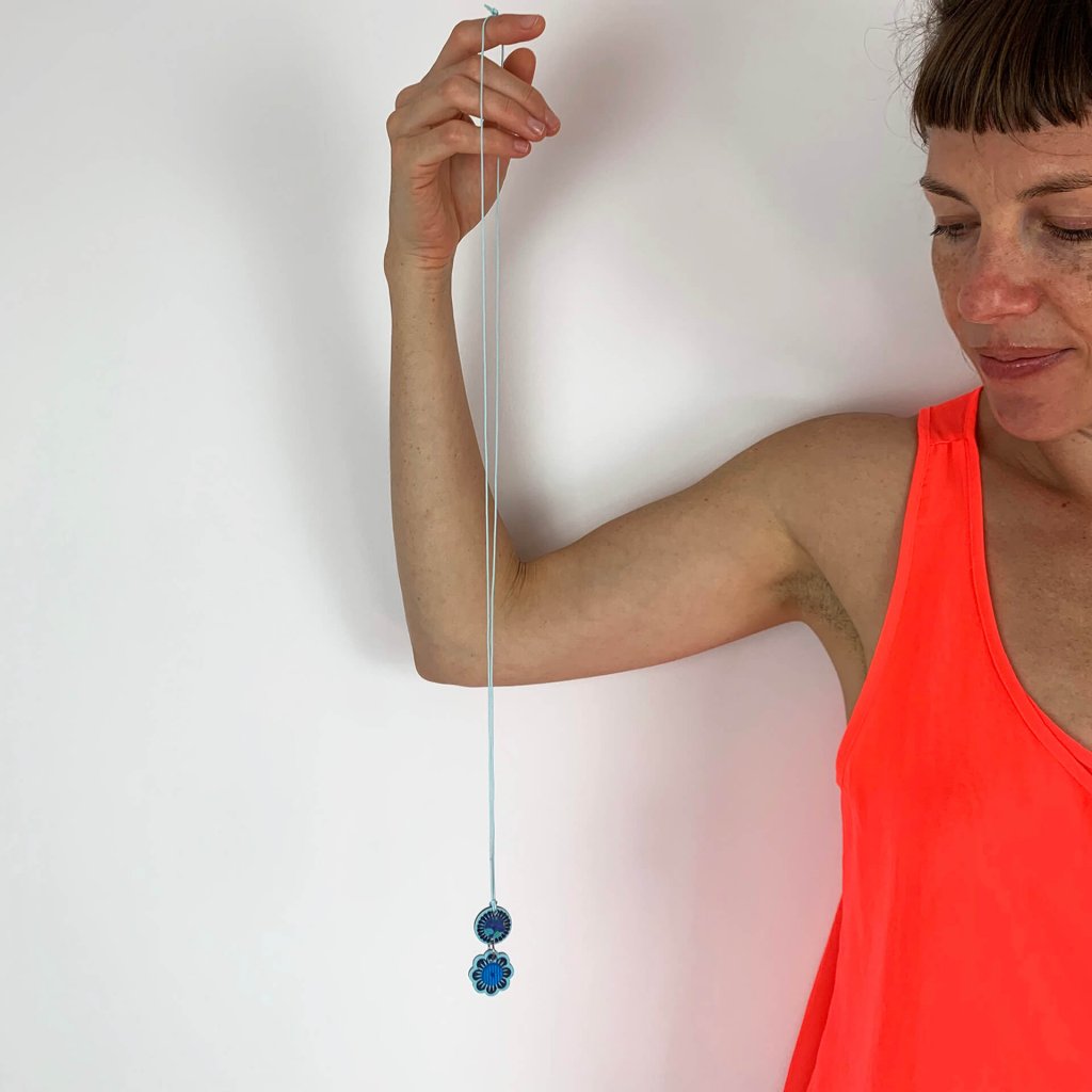 Tiny textile charm pendant necklace with a long blue cord held by a woman in a neon red vest