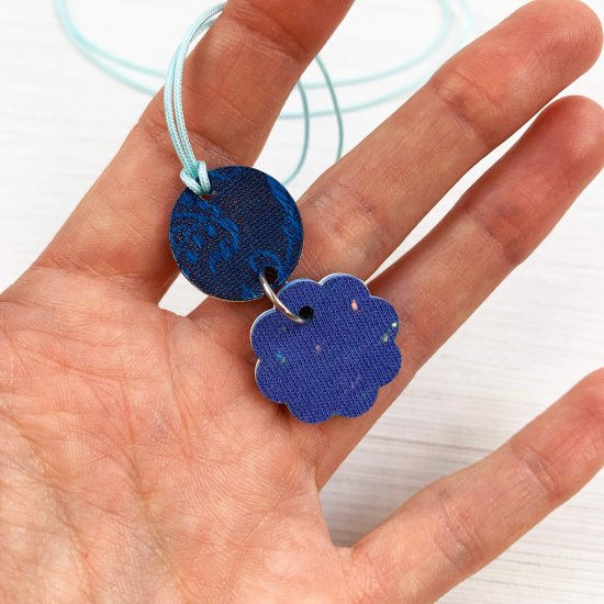 Close up of the reverse side of a charm pendant necklace showing the blue fabric back