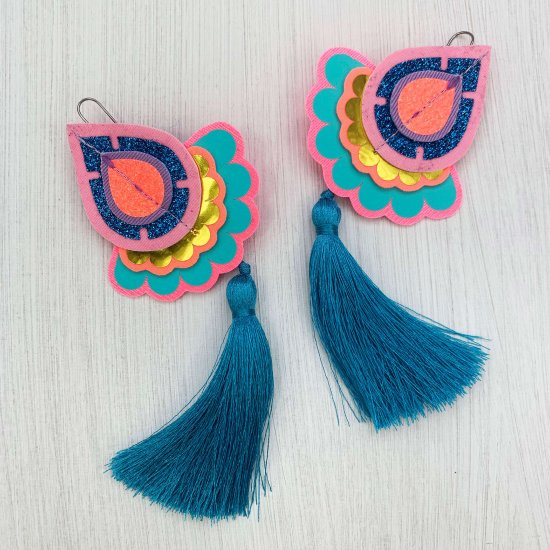 A pair of bright blue, pink and turquoise statement tassel earrings against a plain off white background
