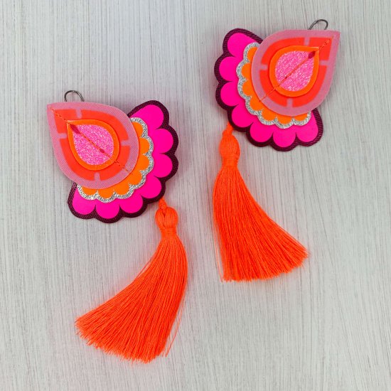 A pair of neon pink, bright orange and purple statement tassel earrings photographed against a plain off white background