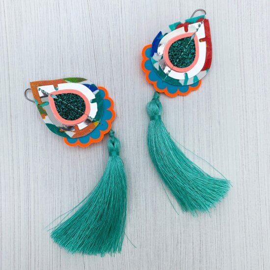 A pair of teardrop shaped Tassel earrings cut from vintage floral fabric, with turquoise green silky tassels seen lying on a plain off white background.