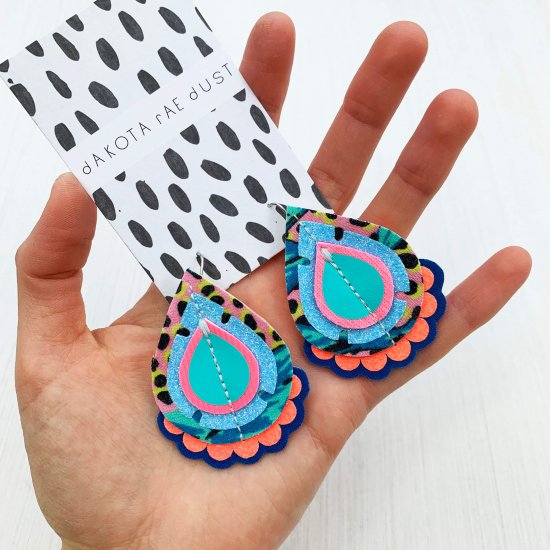 A pair of colourful teardrop earrings held in a woman's open hand