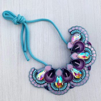 A lilac, light blue and purple statement jewel bib necklace photographed against an off white background
