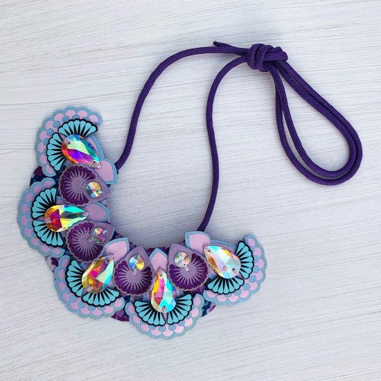 A lilac, light blue and purple statement jewel bib necklace photographed against an off white background