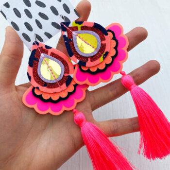 a pair of pink oversize silky tassel earrings are held in an open hand