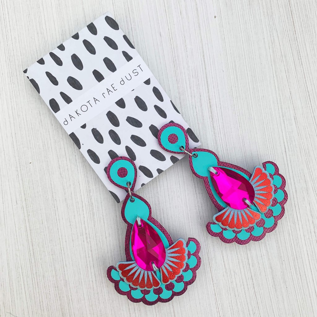 A pair of turquoise, purple and pink statement jewel earrings mounted on a black and white patterned dakota rae dust branded card