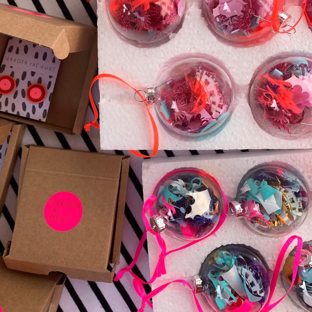A close up photo of two trays of colourful waste vinyl filled glass baubles and some dakota rae dust branded gift boxes
