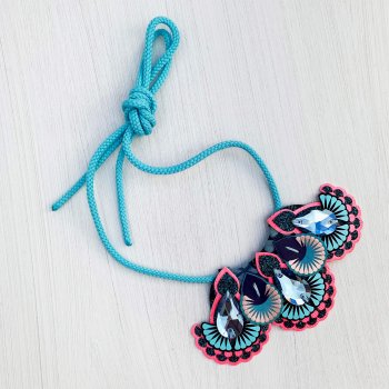 A bight blue and pink jewel mini bib necklace with a light blue cord lying on an off white background