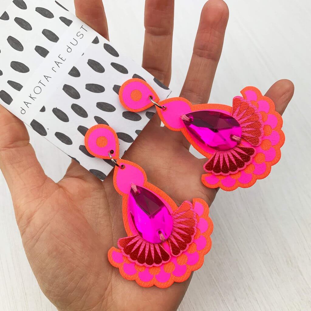 A pair of hot pink jewel earrings are lying on a woman's open palm