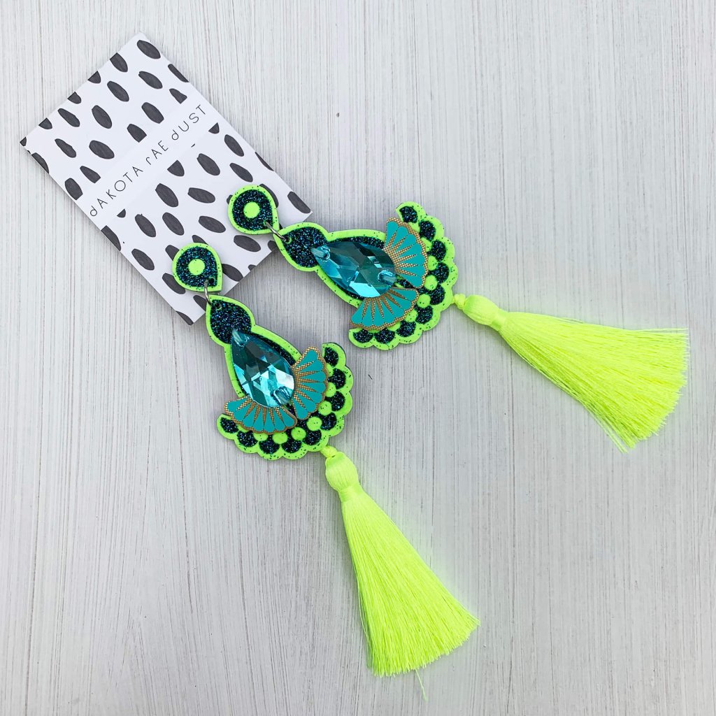 A pair of neon yellow tassel earrings mounted on a dakota rae dust branded card are lying on an off white background