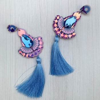A pair of jewelled iridescent silky tassel earrings in lavender and soft blue are seen against an off white background
