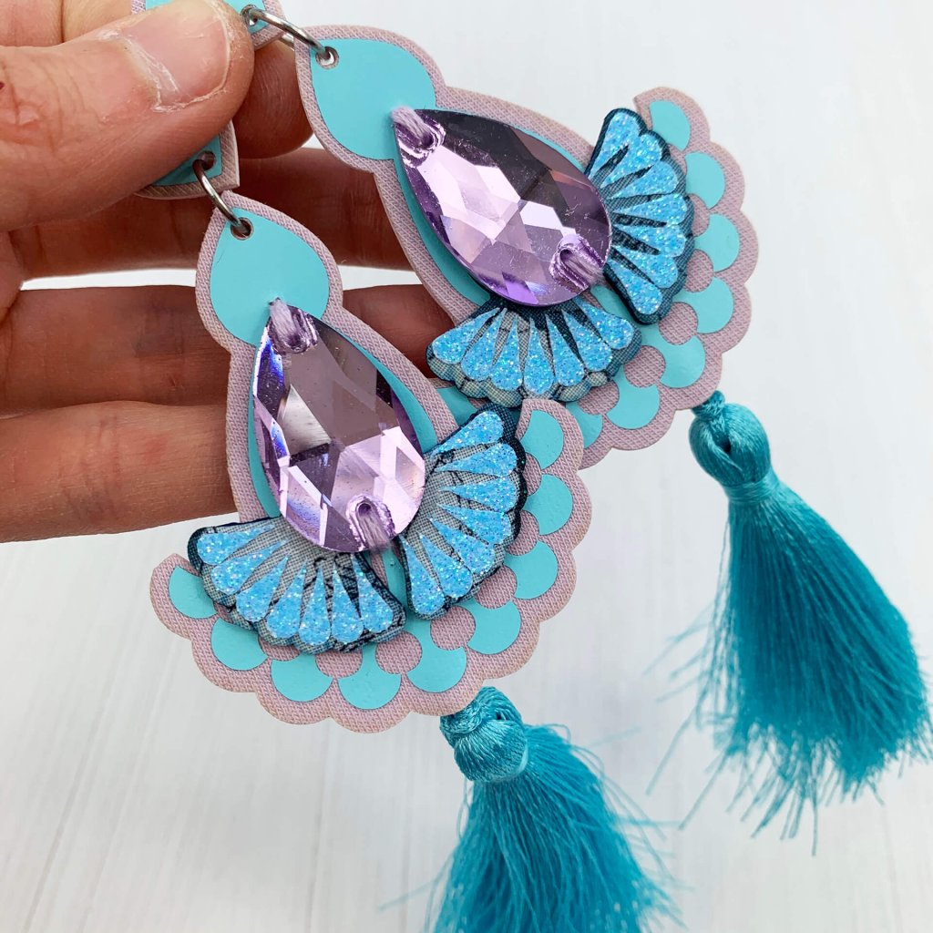 A pair of lilac and light blue statement tassel earrings with lilac jewels lying on a woman's open palm
