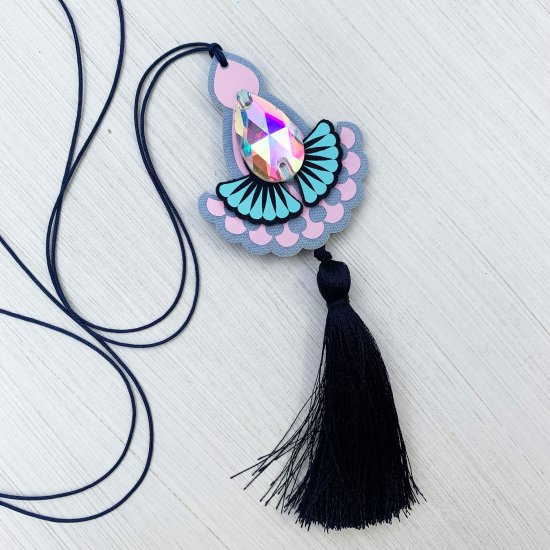 A lilac and light blue jewelled tassel pendant necklace with navy cord and navy tassel lies on an off white background
