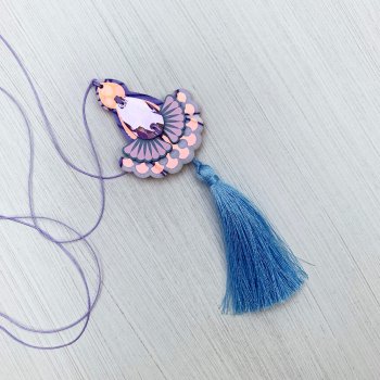 A floral print, iridescent and lavender jewelled tassel pendant necklace with lilac cord and soft blue tassel lies on an off white background