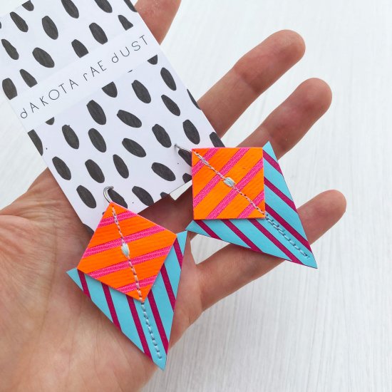 A bright and colourful pair of graphic stripe earrings in bright orange, light blue and pink and held out for the camera in an open hand