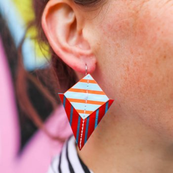 A close up of a woman's ear and stripey triangle earrings. Behind her is some colourful graffiti.