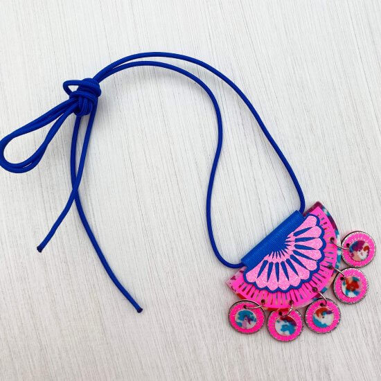 A royal blue and bright pink jangling charm necklace is lying on an off white textured background