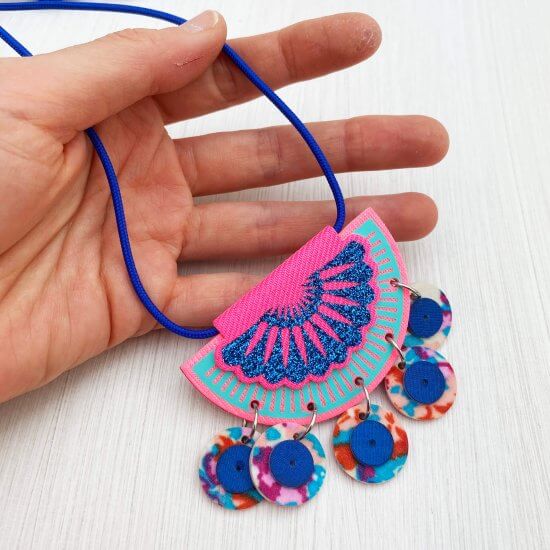 A close up of a blue and pink jangling charm necklace held in the open palm of a white hand.