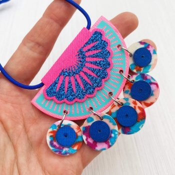 A close up of a blue and pink jangling charm necklace held in the open palm of a white hand.