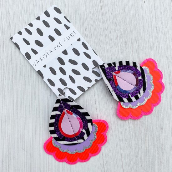 A pair of oversize teardrop earrings mounted on a dakota rae dust branded card.