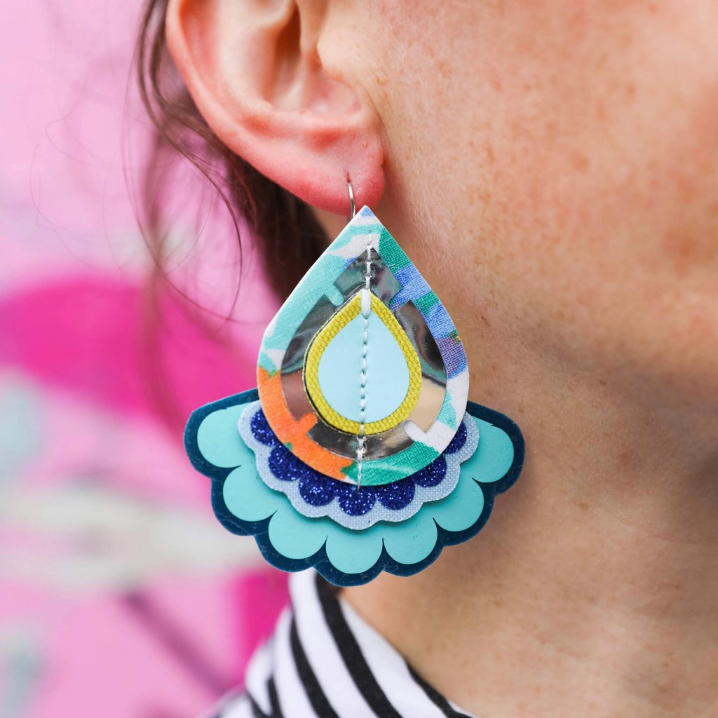 A close up of a white woman's ear. She is wearing a ornate looking teardrop shaped earring in blue and turquoise.