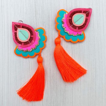 A pair of bright and colourful, orange, pink and turquoise oversize tassel earrings lying on an off white textured background