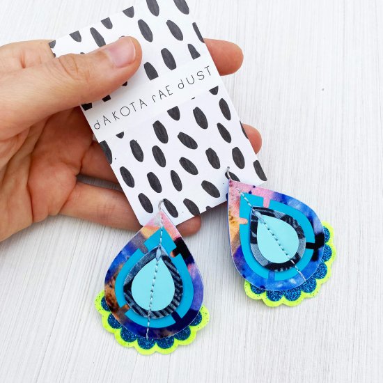 A pair of colourful recycled fabric earrings in blue and lime green held in a woman's open hand