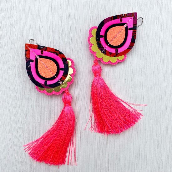 A pair of fluorescent pink and gold, vintage fabric tassel earrings are lying on an off white background