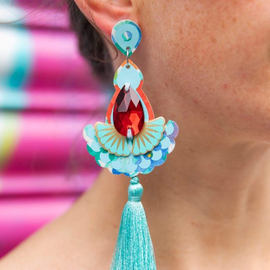 A close up of a woman's neck and ear focusing on her turquoise tassel earrings adorned with red teardrop shaped jewels