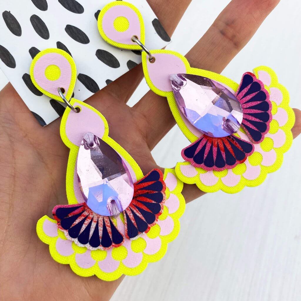A pair of yellow lilac statement earrings held in a woman's open hand