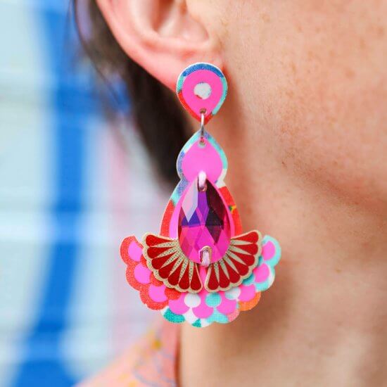 A close up of a white woman's ear and colourful hot pink jewel earrings
