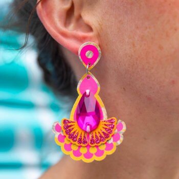 A close up of a woman's ear and neck, focusing on the yellow pink dangly earrings she is wearing