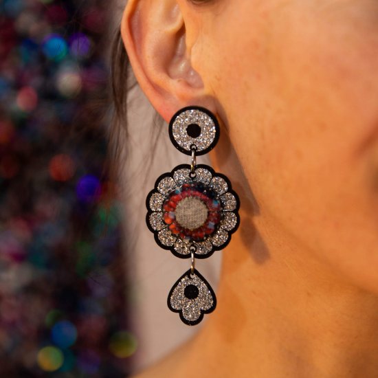 A close up of a woman's neck and ear focusing on her black and silver glitter dangly charm earrings