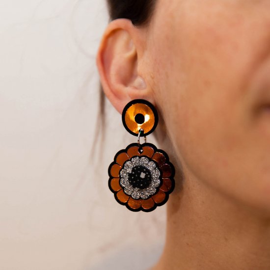 A close up of a woman's ear and neck focusing on her iridescent floral motif earrings