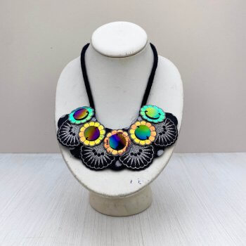 An ornate iridescent bib necklace displayed on an off white mannequin neck is sitting in front of an off white background