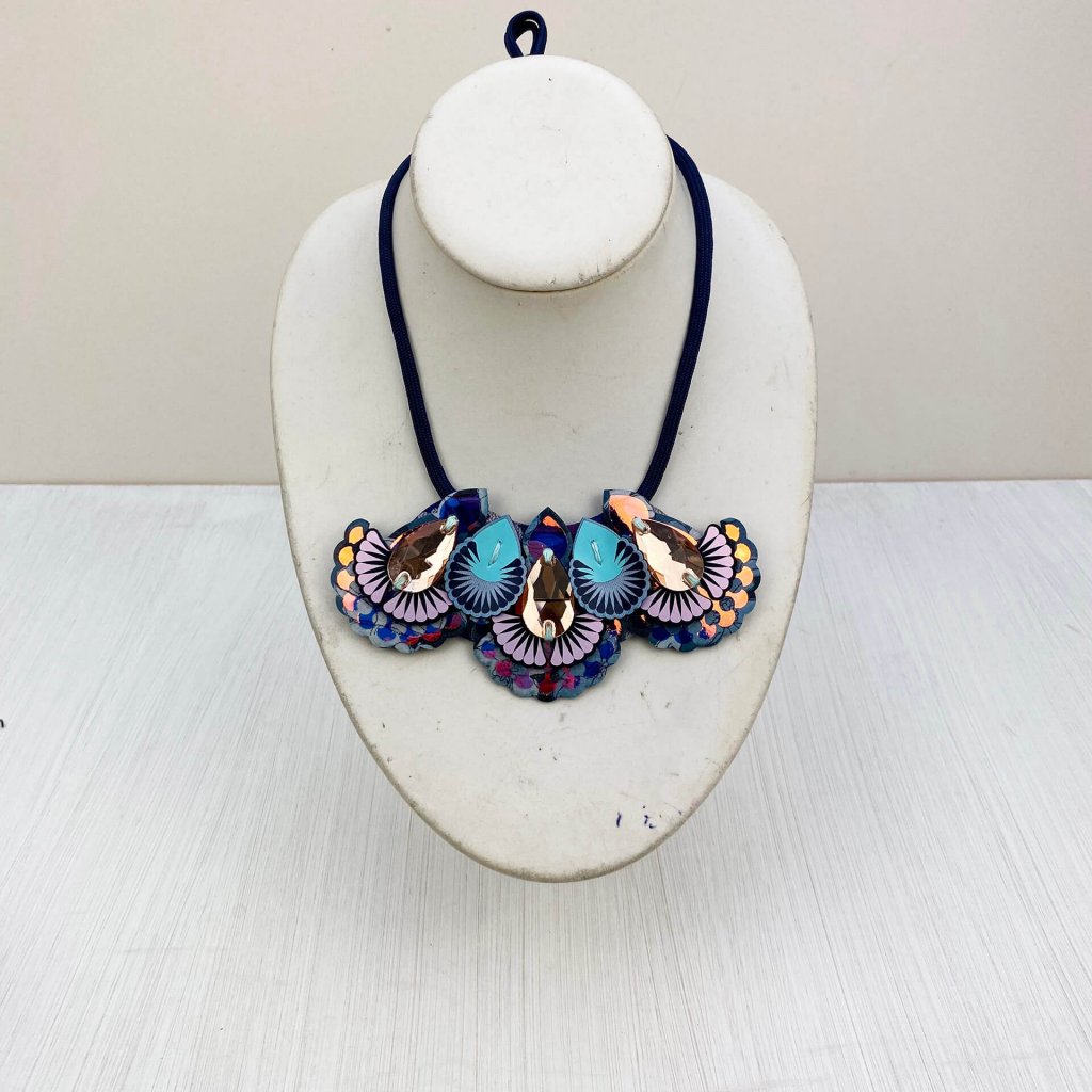An ornate iridescent mini bib necklace is displayed on a n off white mannequin neck