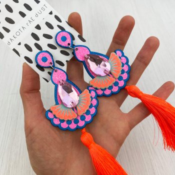 A pair of blue, pink and orange jewel tassel earrings are held in an open hand