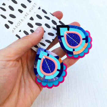A pair of blue and peach recycled fabric earrings held in a open hand
