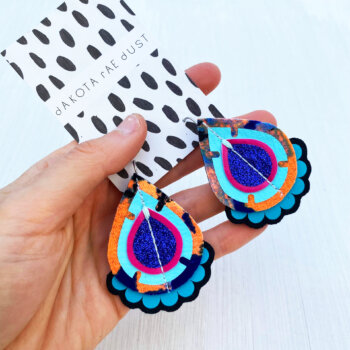 A pair of blue and orange recycled fabric earrings held in a open hand