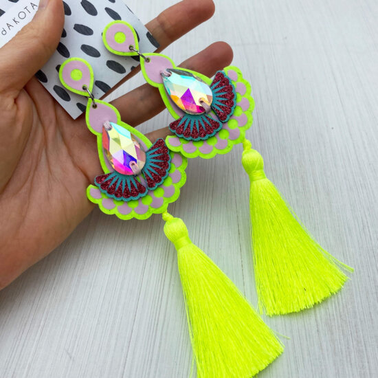 A pair of luxury fluorescent yellow tassel earrings are held in an open hand