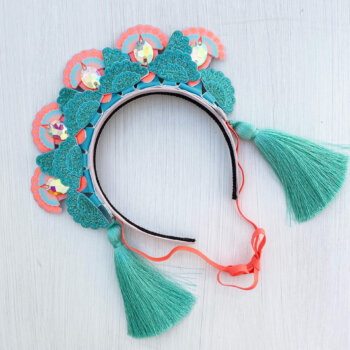 A mint green and peach 5 jewel tiara style tasselled headdress is lying on an off white background
