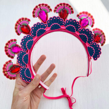 A colourful 7 jewel halo headdress held in a woman's hand against an off white background