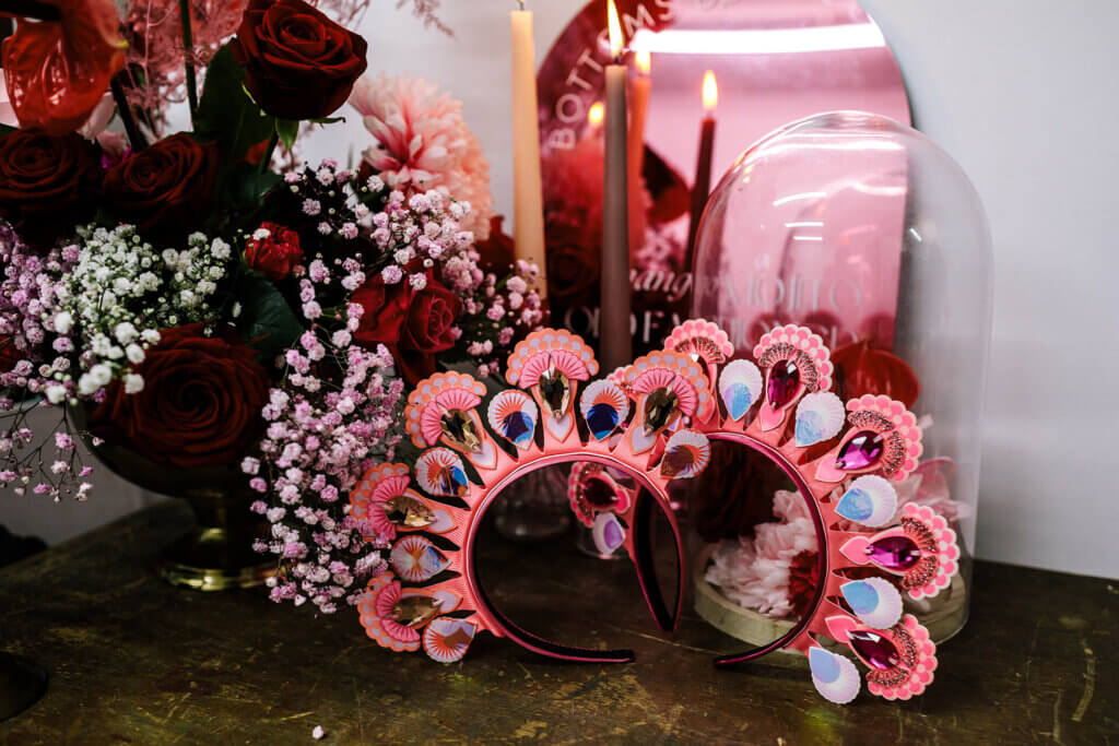 A pair of jewelled bridal headdresses rest against a pink mirror, and large bouquet of pink and red flowers.