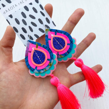A pair of pink and blue recycled floral fabric tassel earrings are held in an open hand