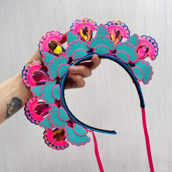 A 7 jewel headdress in turquoise and pink is held in a hand against an off white background
